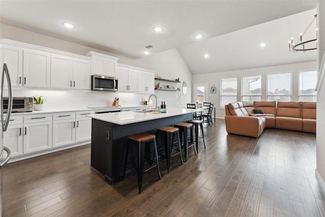 kitchen with an island with sink, white cabinetry, stainless steel microwave, and light countertops