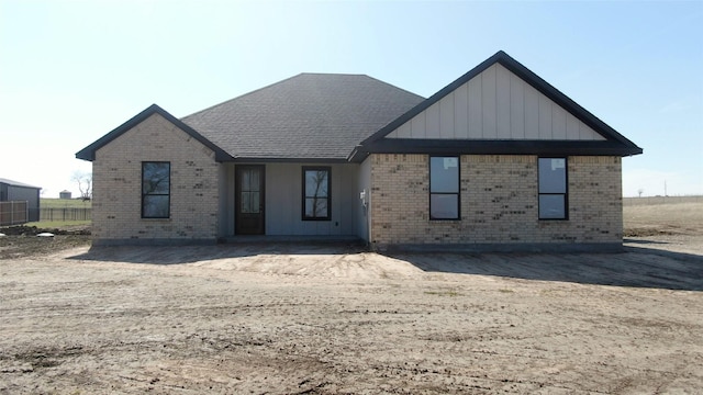 view of front of house with board and batten siding, brick siding, and a shingled roof