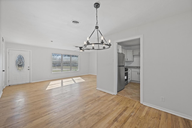 unfurnished dining area featuring ceiling fan with notable chandelier and light hardwood / wood-style flooring