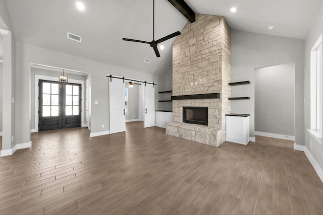 unfurnished living room with a barn door, visible vents, beamed ceiling, high vaulted ceiling, and ceiling fan