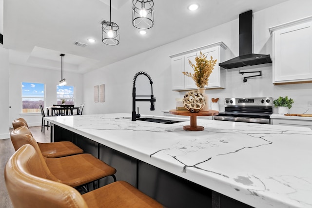 kitchen with pendant lighting, wall chimney range hood, a breakfast bar, stainless steel range with electric stovetop, and white cabinetry