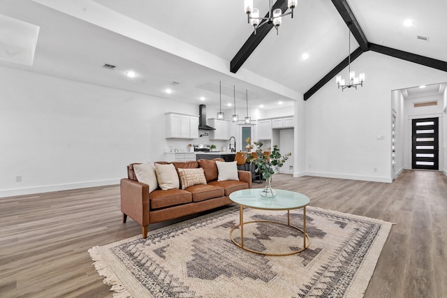 living room featuring sink, beam ceiling, light hardwood / wood-style flooring, and a chandelier