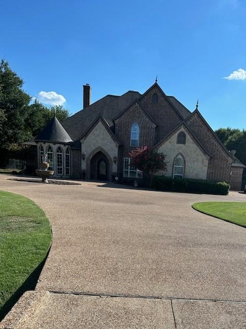 french provincial home featuring stone siding, a front lawn, and a chimney