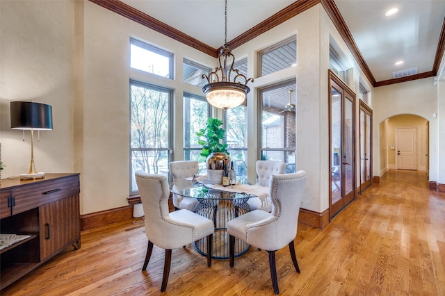 dining area with crown molding, a towering ceiling, a chandelier, and light hardwood / wood-style flooring