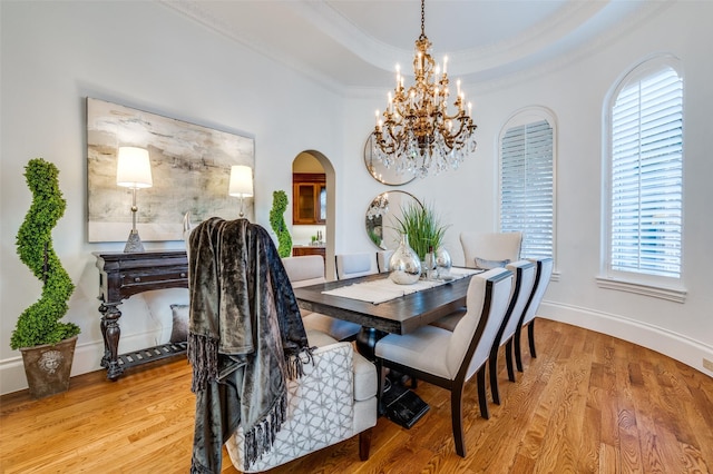 dining area with an inviting chandelier, ornamental molding, a tray ceiling, and light hardwood / wood-style flooring