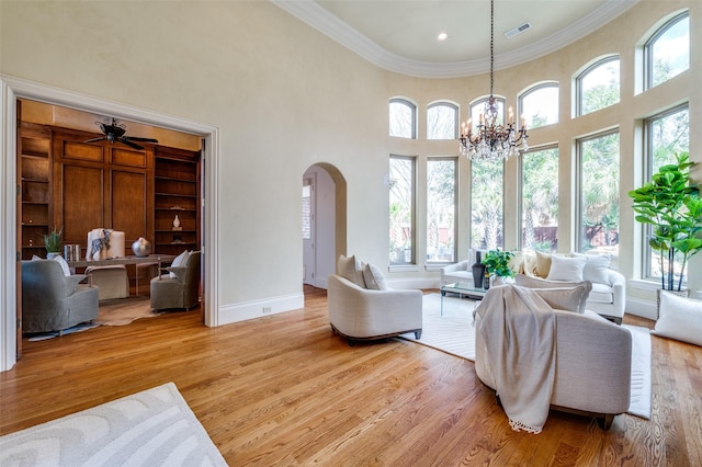 living room with crown molding, a chandelier, light hardwood / wood-style floors, and a high ceiling