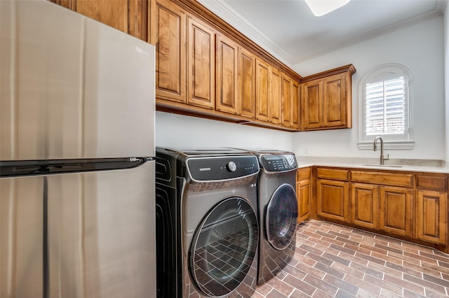 clothes washing area with sink, crown molding, cabinets, and washer and dryer