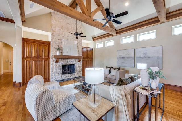 living room with high vaulted ceiling, beam ceiling, light hardwood / wood-style floors, and a stone fireplace