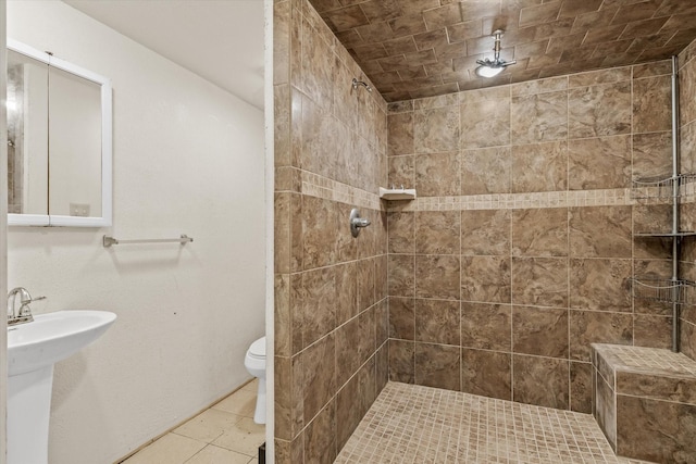 bathroom with toilet, tile patterned flooring, and a tile shower