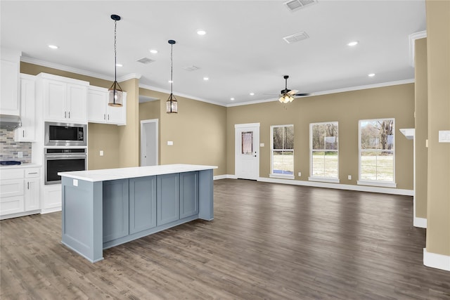 kitchen with a kitchen island, appliances with stainless steel finishes, pendant lighting, white cabinets, and backsplash