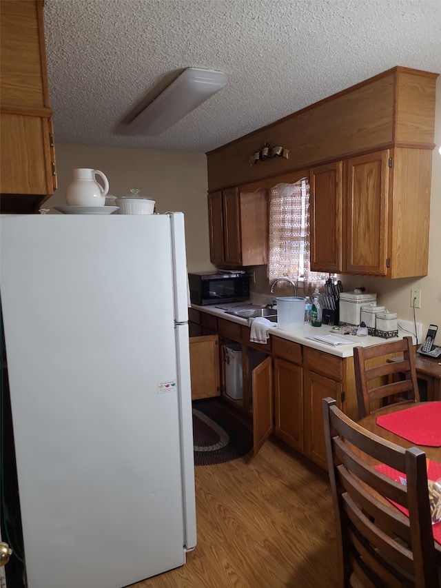 kitchen with white refrigerator, sink, light hardwood / wood-style floors, and a textured ceiling