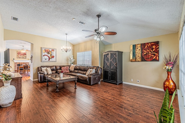 living room with vaulted ceiling, a textured ceiling, dark hardwood / wood-style flooring, a fireplace, and ceiling fan with notable chandelier