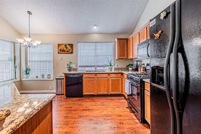 kitchen with light stone counters, lofted ceiling, light wood-type flooring, and black appliances