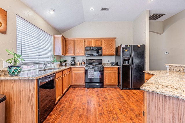 kitchen with lofted ceiling, sink, light stone counters, light hardwood / wood-style flooring, and black appliances