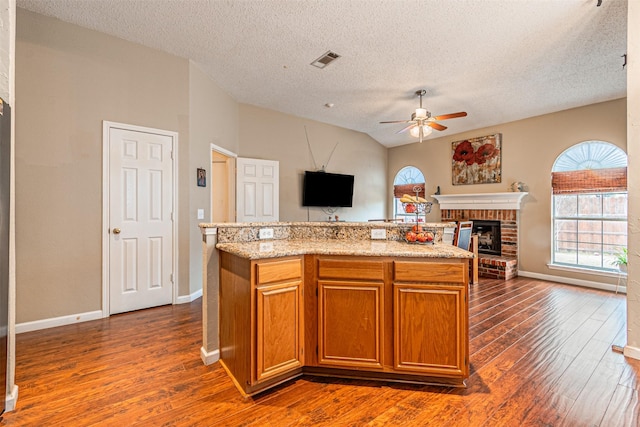 kitchen featuring ceiling fan, dark hardwood / wood-style flooring, a brick fireplace, and a kitchen island