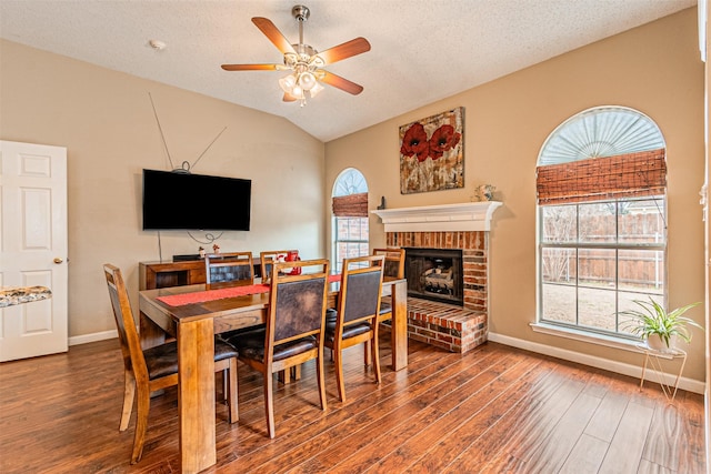 dining area featuring lofted ceiling, wood-type flooring, a brick fireplace, and a wealth of natural light