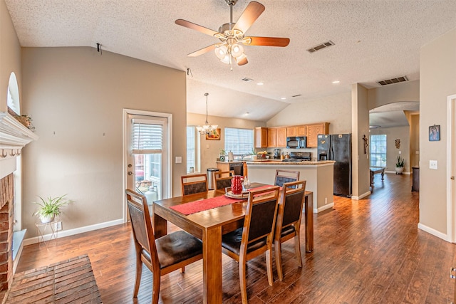 dining space featuring lofted ceiling, ceiling fan with notable chandelier, a textured ceiling, and dark hardwood / wood-style flooring