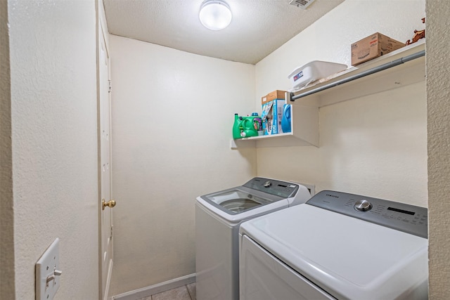 laundry room with washing machine and dryer, light tile patterned flooring, and a textured ceiling