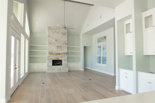 unfurnished living room featuring light wood-style floors, a fireplace, high vaulted ceiling, and built in shelves