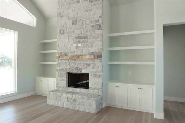 unfurnished living room with light wood finished floors, a stone fireplace, and built in shelves