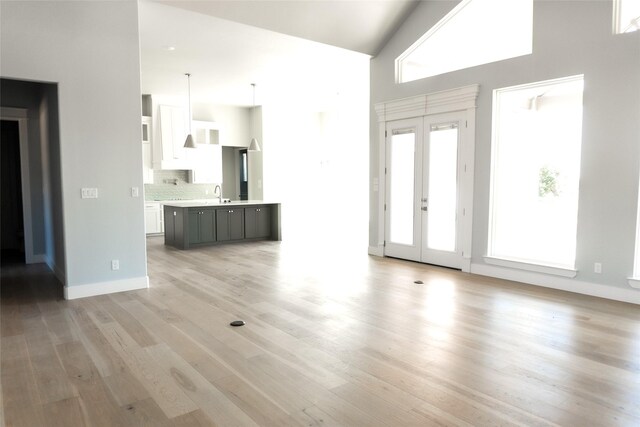 unfurnished living room featuring light wood finished floors, baseboards, a towering ceiling, french doors, and a sink