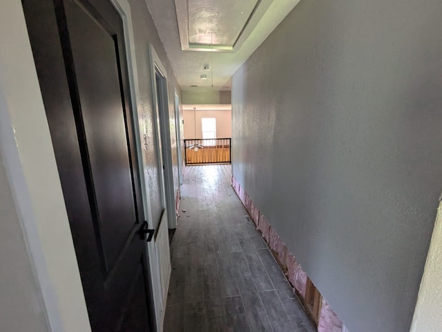 corridor with a textured wall, dark wood-type flooring, baseboards, and attic access