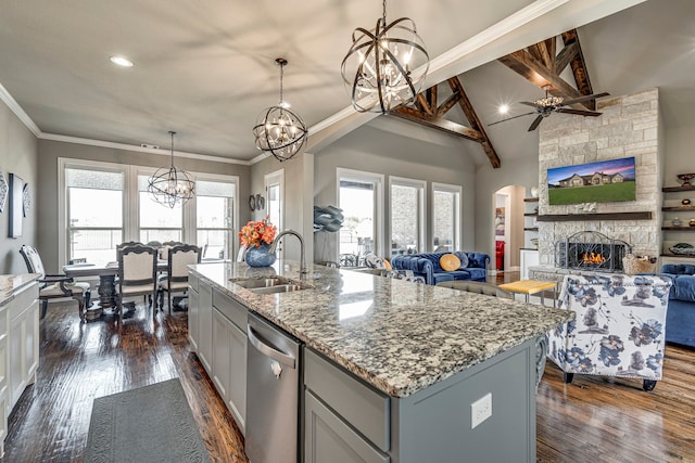 kitchen featuring sink, light stone counters, decorative light fixtures, stainless steel dishwasher, and a kitchen island with sink