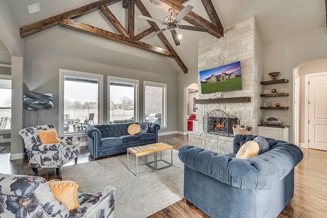 living room featuring beam ceiling, a stone fireplace, wood-type flooring, and high vaulted ceiling