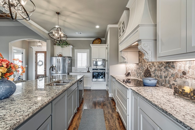 kitchen featuring sink, backsplash, stainless steel appliances, white cabinets, and decorative light fixtures