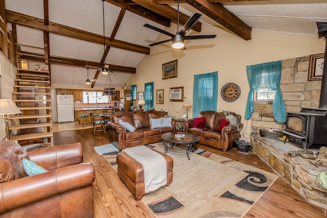 living room with ceiling fan, high vaulted ceiling, light hardwood / wood-style floors, and a wood stove