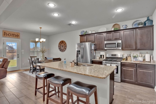 kitchen featuring light stone countertops, dark brown cabinets, stainless steel appliances, and an island with sink