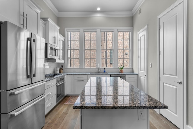 kitchen with white cabinets, appliances with stainless steel finishes, a kitchen island, and dark stone countertops