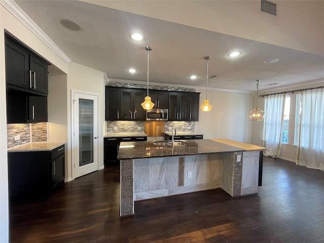 kitchen featuring pendant lighting, sink, ornamental molding, and a center island with sink