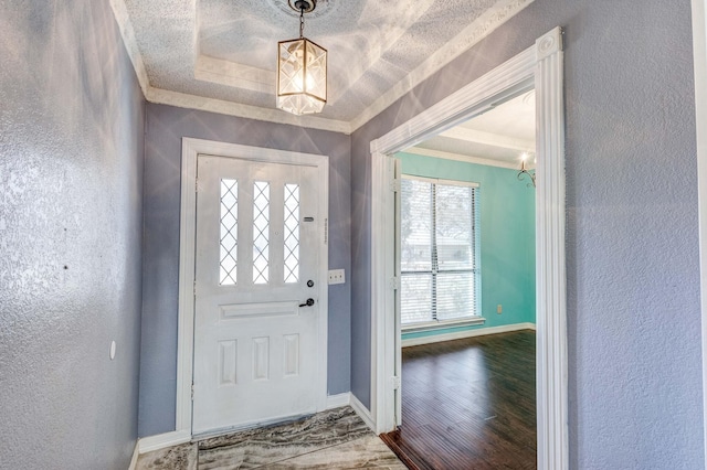 entrance foyer with hardwood / wood-style flooring, ornamental molding, a raised ceiling, and a textured ceiling