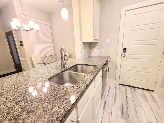 kitchen featuring sink, dishwasher, white cabinetry, dark stone countertops, and decorative light fixtures