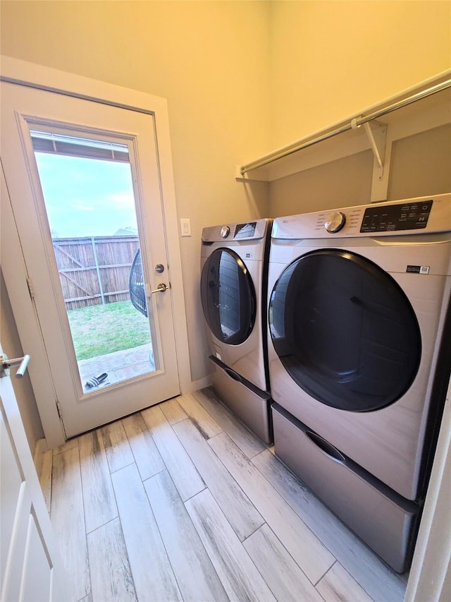 clothes washing area with washing machine and dryer and light wood-type flooring