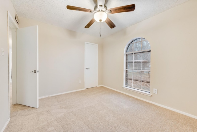 empty room with ceiling fan, light colored carpet, and a textured ceiling