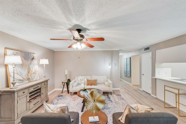 living room featuring ceiling fan, crown molding, light hardwood / wood-style floors, and a textured ceiling