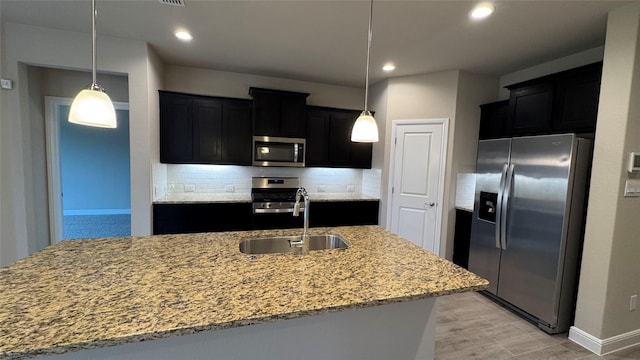 kitchen featuring appliances with stainless steel finishes, sink, hanging light fixtures, and a center island with sink