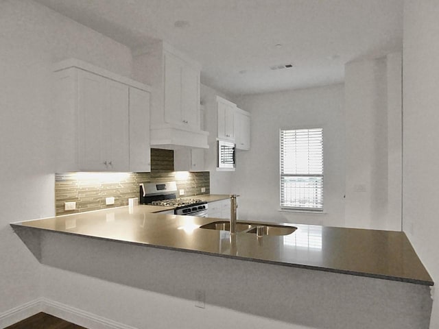 kitchen with sink, white cabinets, backsplash, kitchen peninsula, and gas range