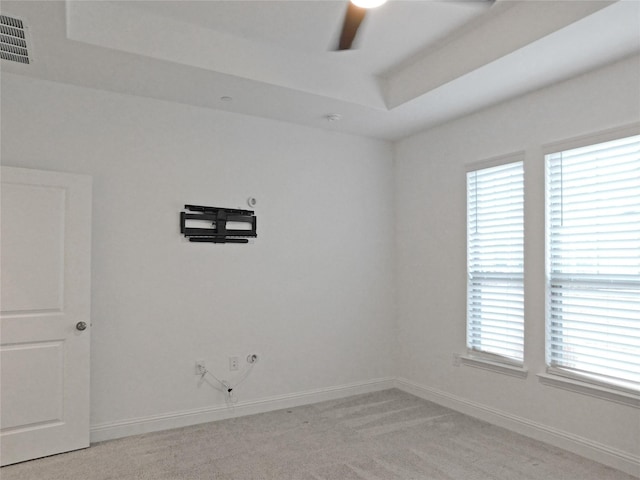 empty room with a raised ceiling, a healthy amount of sunlight, light carpet, and ceiling fan