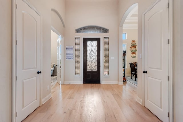 entrance foyer featuring arched walkways, baseboards, a towering ceiling, and light wood-style floors