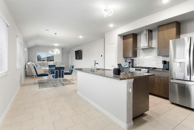 kitchen with sink, stainless steel fridge, backsplash, wall chimney range hood, and a center island with sink