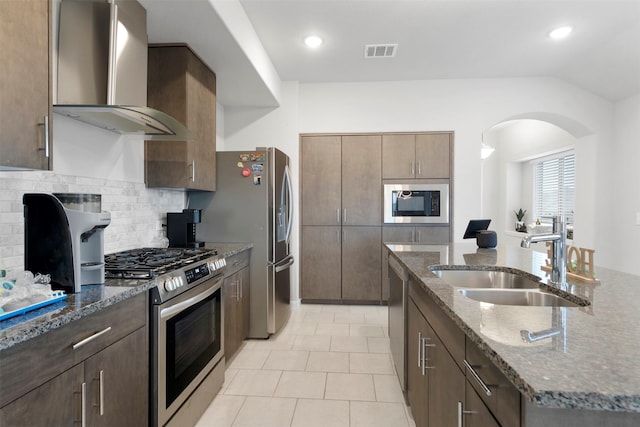 kitchen with lofted ceiling, sink, dark stone countertops, stainless steel appliances, and wall chimney exhaust hood