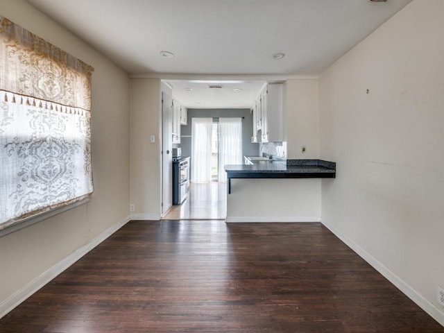 kitchen with white cabinetry, sink, stainless steel range, kitchen peninsula, and dark wood-type flooring