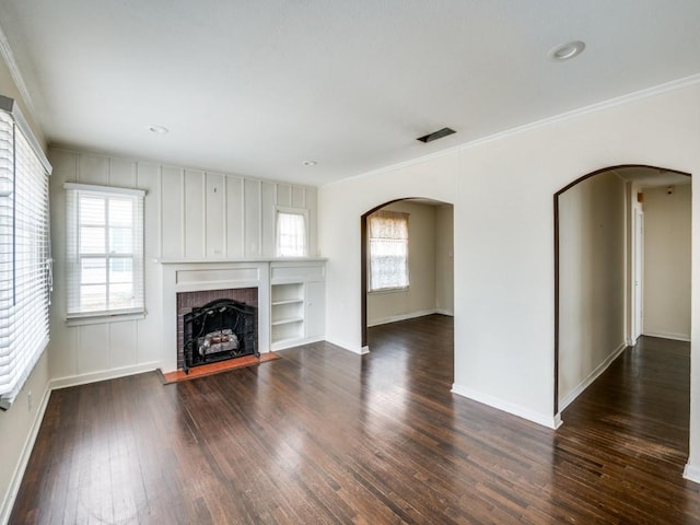 unfurnished living room featuring dark hardwood / wood-style floors, ornamental molding, a fireplace, and a wealth of natural light