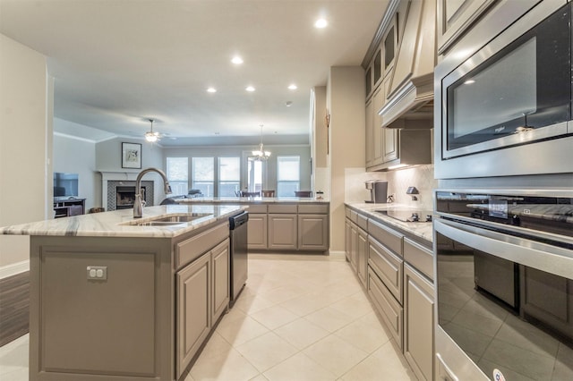 kitchen with tasteful backsplash, an island with sink, sink, light stone counters, and stainless steel appliances