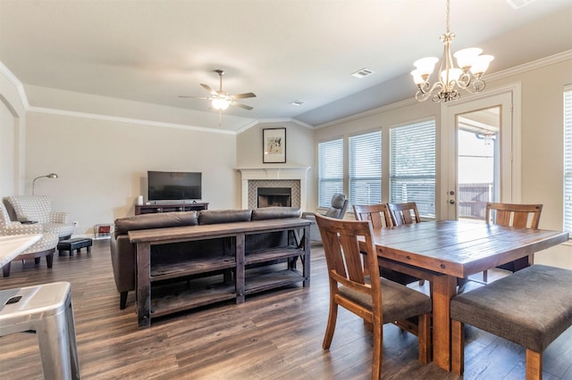 dining space with ornamental molding, dark hardwood / wood-style flooring, ceiling fan with notable chandelier, and a tile fireplace