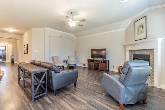 living room with a tiled fireplace, ornamental molding, ceiling fan, and dark hardwood / wood-style flooring