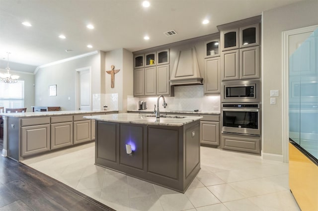 kitchen with premium range hood, sink, appliances with stainless steel finishes, kitchen peninsula, and a kitchen island with sink